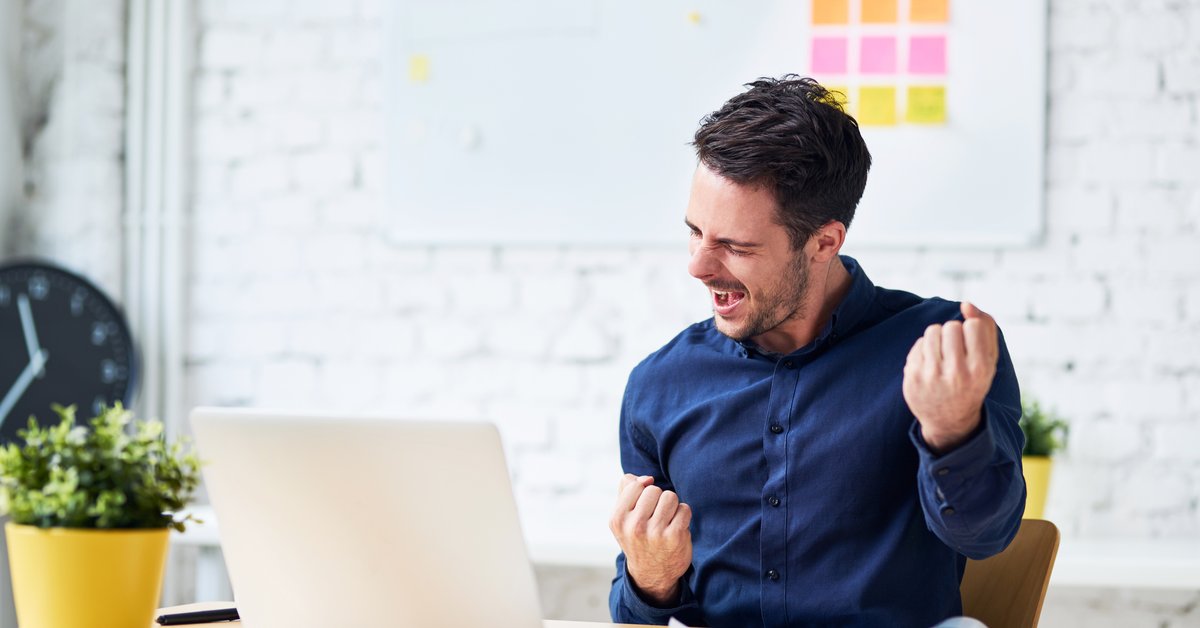 Man sitting at a desk celebrating with a fist pump