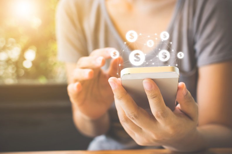 Person holding their smartphone with a graphic of a web of dollar signs coming from the top of the phone.