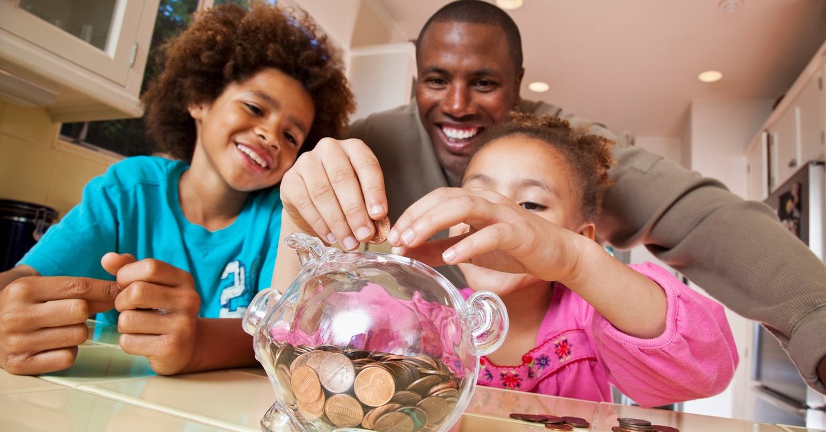 A parent watches their children put coins into a piggy bank at home.