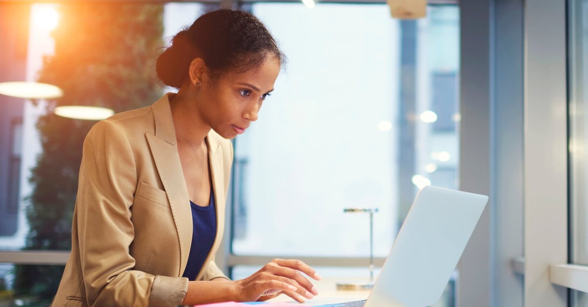 A woman in business attire looking intently at her laptop screen.