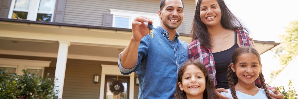 A husband, wife, and two daughters stand outside a home holding house keys.