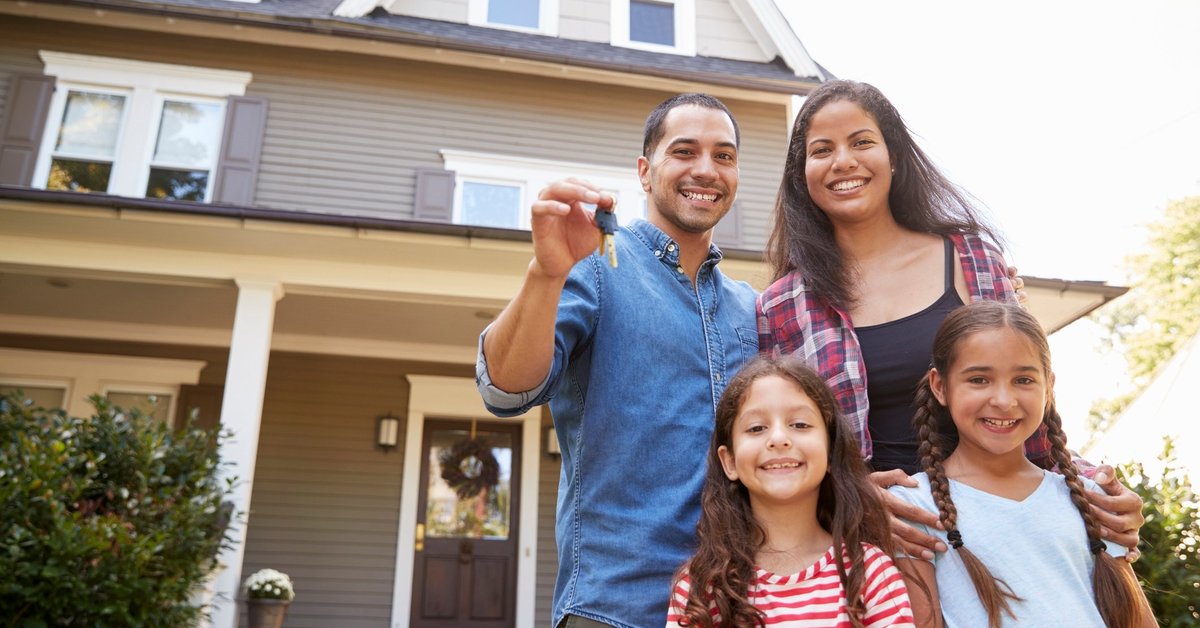 A husband, wife, and two daughters stand outside a home holding house keys.