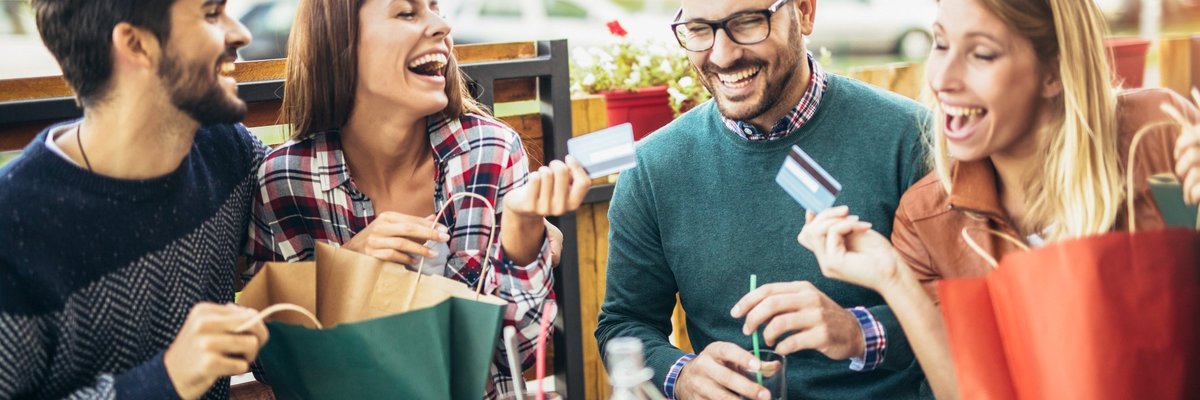 Group of young men and women laughing at table holding credit cards