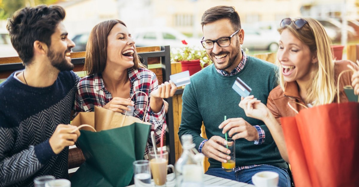 Group of young men and women laughing at table holding credit cards