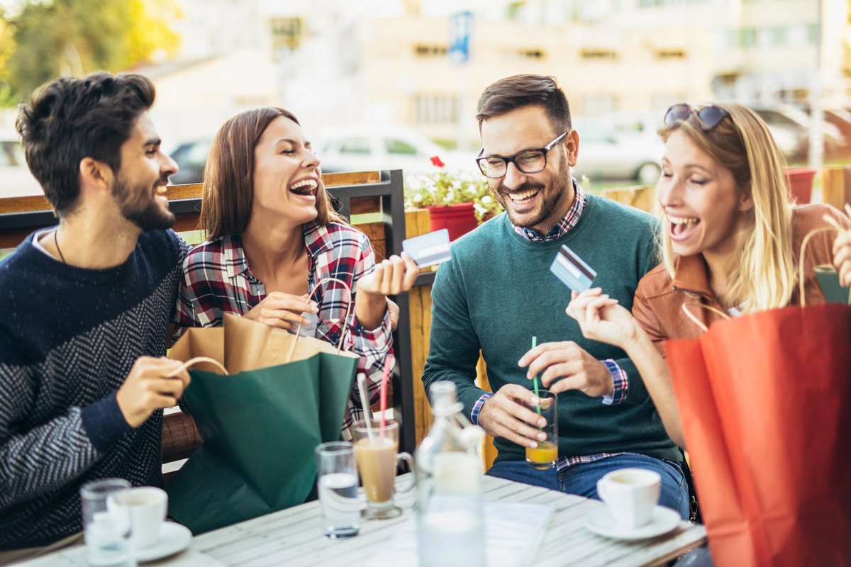 Group of young men and women laughing at table holding credit cards