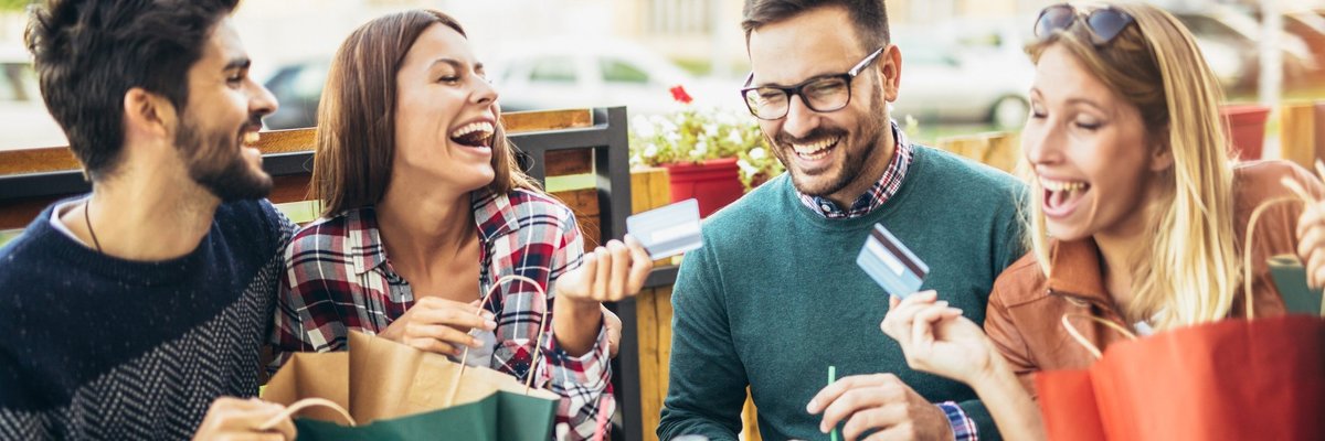 Group of young men and women laughing at table holding credit cards