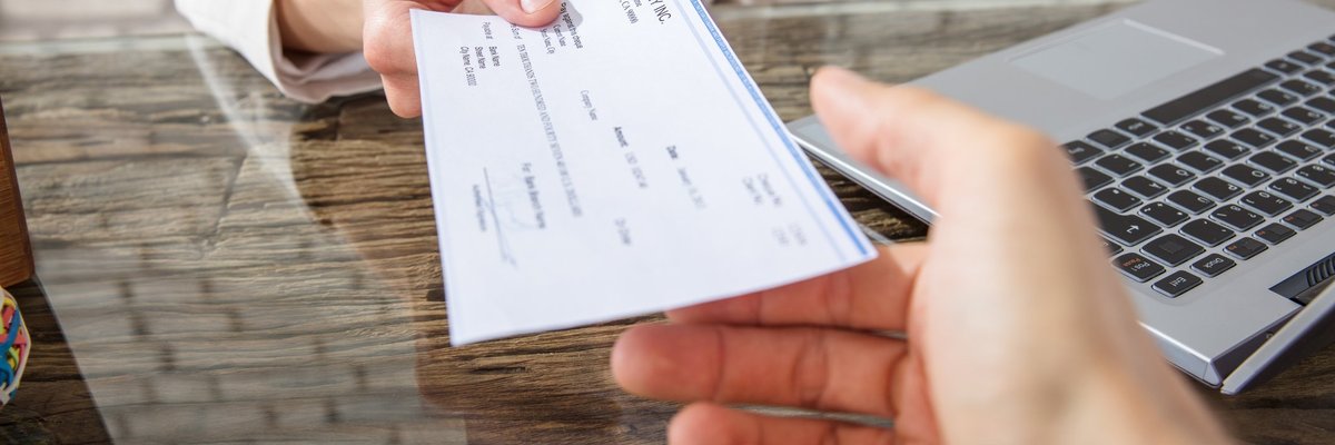 One hand passing a check to another across a desk.