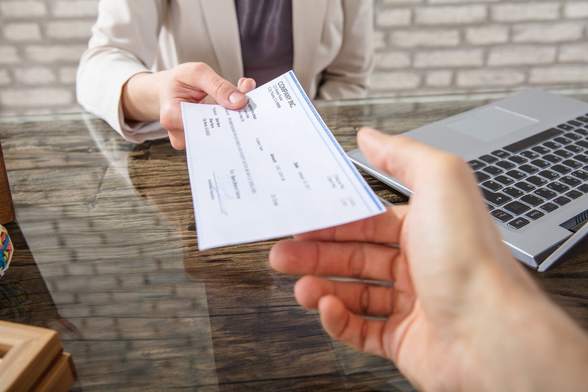 One hand passing a check to another across a desk.