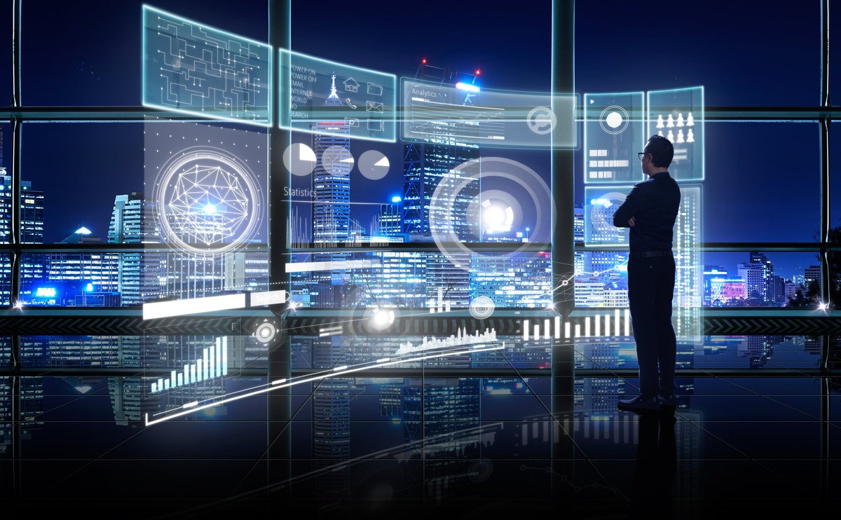 Bespectacled man in black looking at complex network of hologram screens.