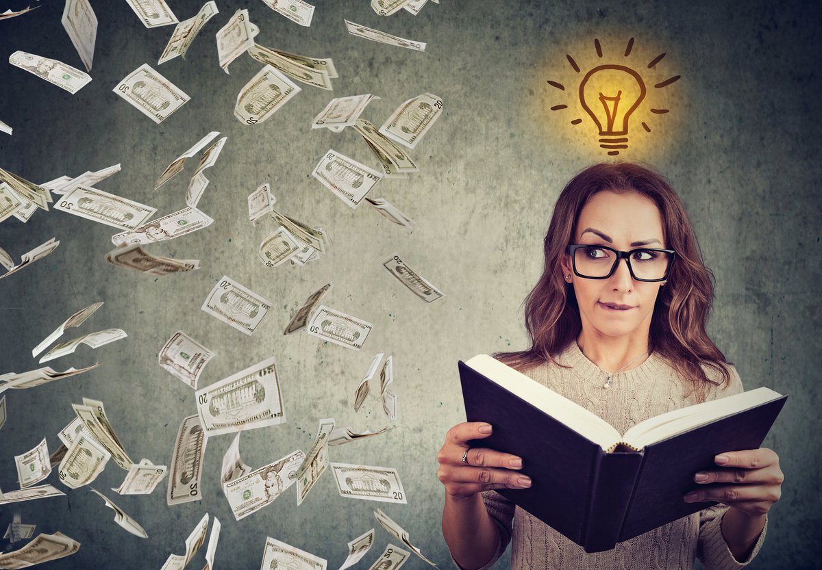 Bespectacled woman opening book and looking over at raining money.