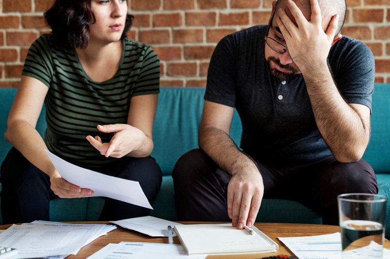 frustrated man and woman sitting on couch looking at paperwork