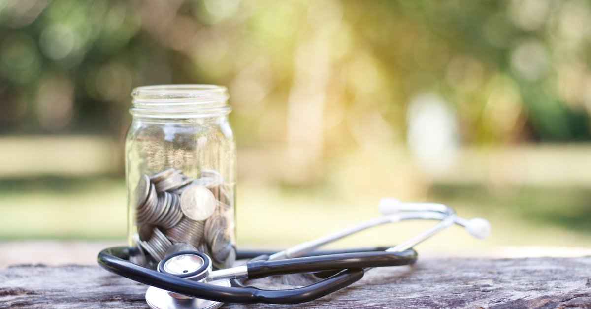 A jar full of coins sits with a stethoscope on top of a log outdoors.