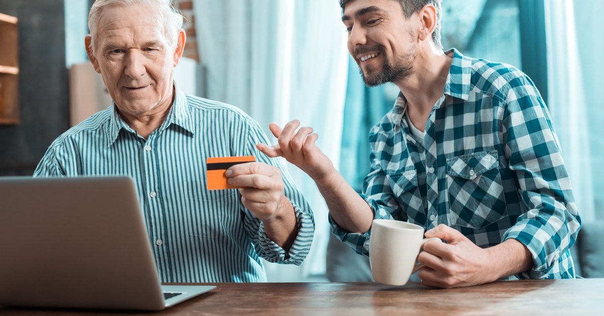 Baby boomer holding credit card beside smiling millennial.
