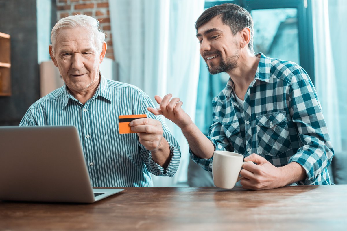 Baby boomer holding credit card beside smiling millennial.