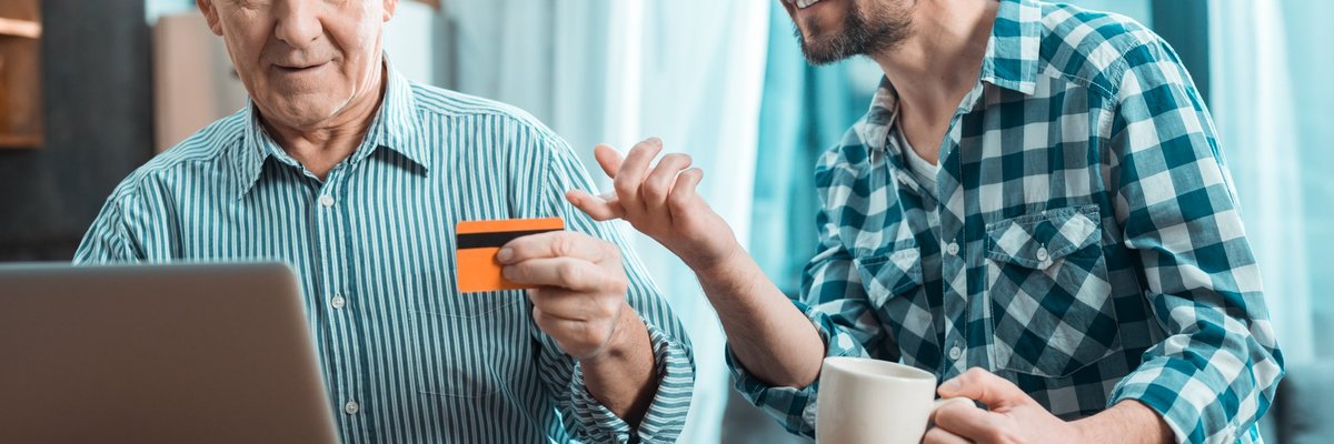 Baby boomer holding credit card beside smiling millennial.