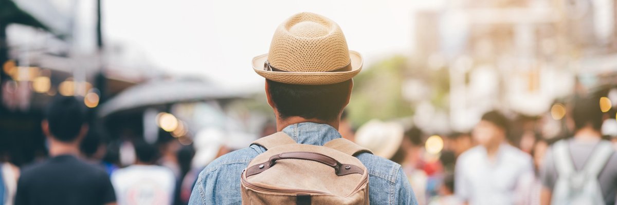 Man in backpack and straw hat facing away while walking into throng of locals in exotic locale.