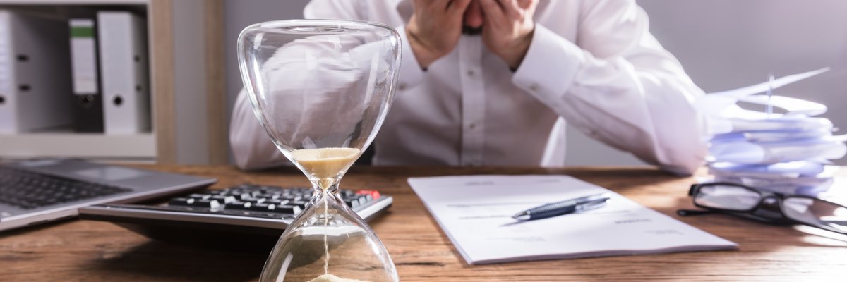 Person has there head in their hands at desk with an hourglass and calculator in the foreground.