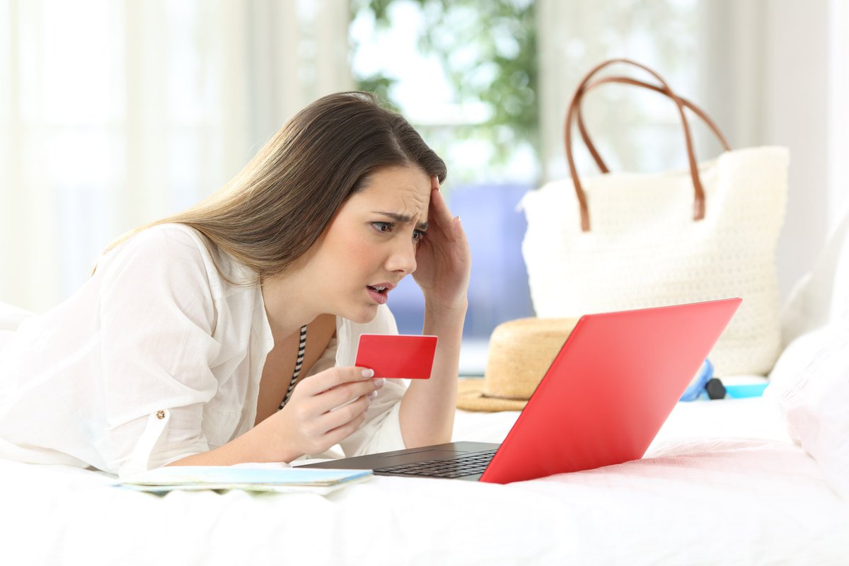 Young woman holding credit card and looking at computer screen in distress.