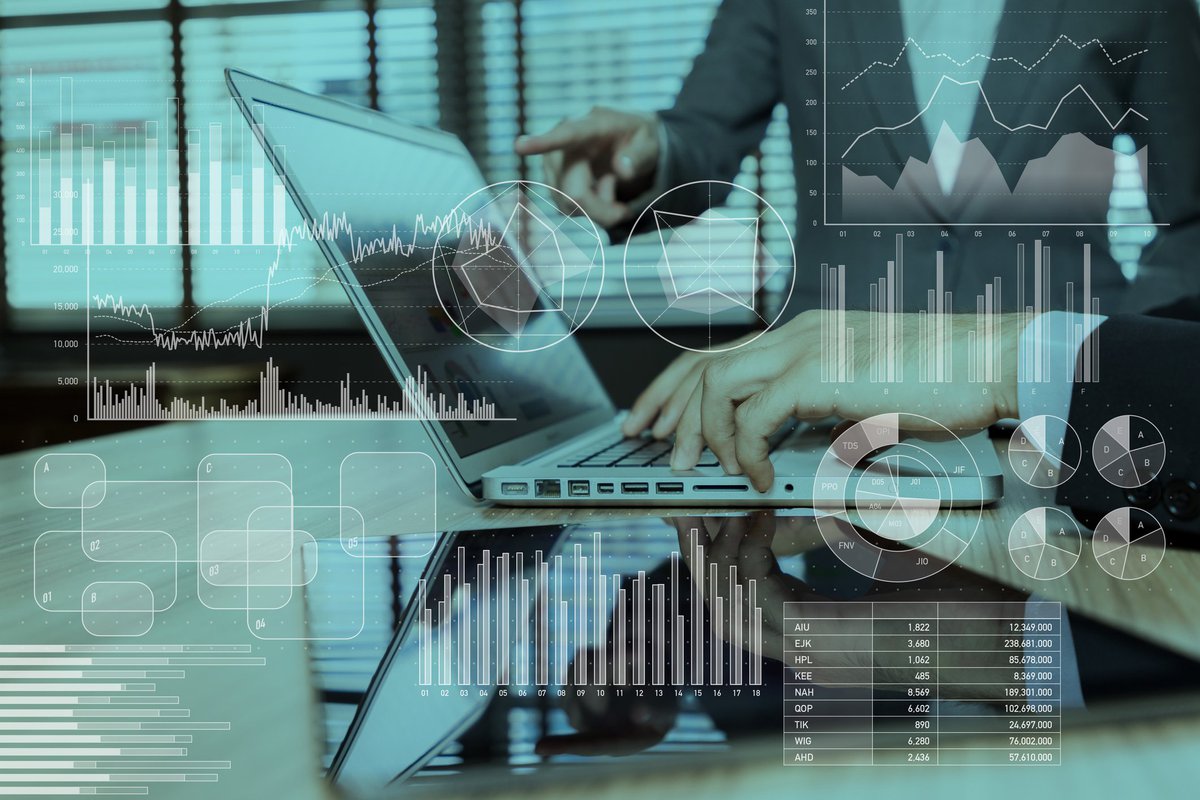 Holograms of charts and graphs over someone pointing at a laptop screen while another person types.