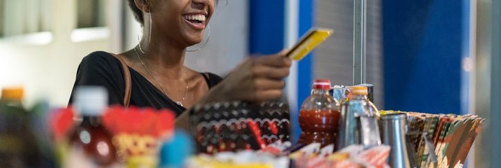 A young woman buys food from a street vendor using a credit card.
