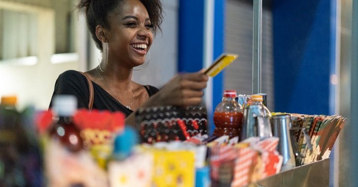 A young woman buys food from a street vendor using a credit card.