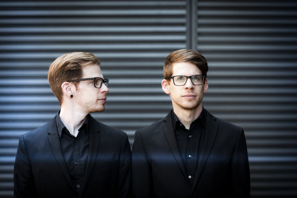 Two men who appear to be the same person standing side by side in black suits.