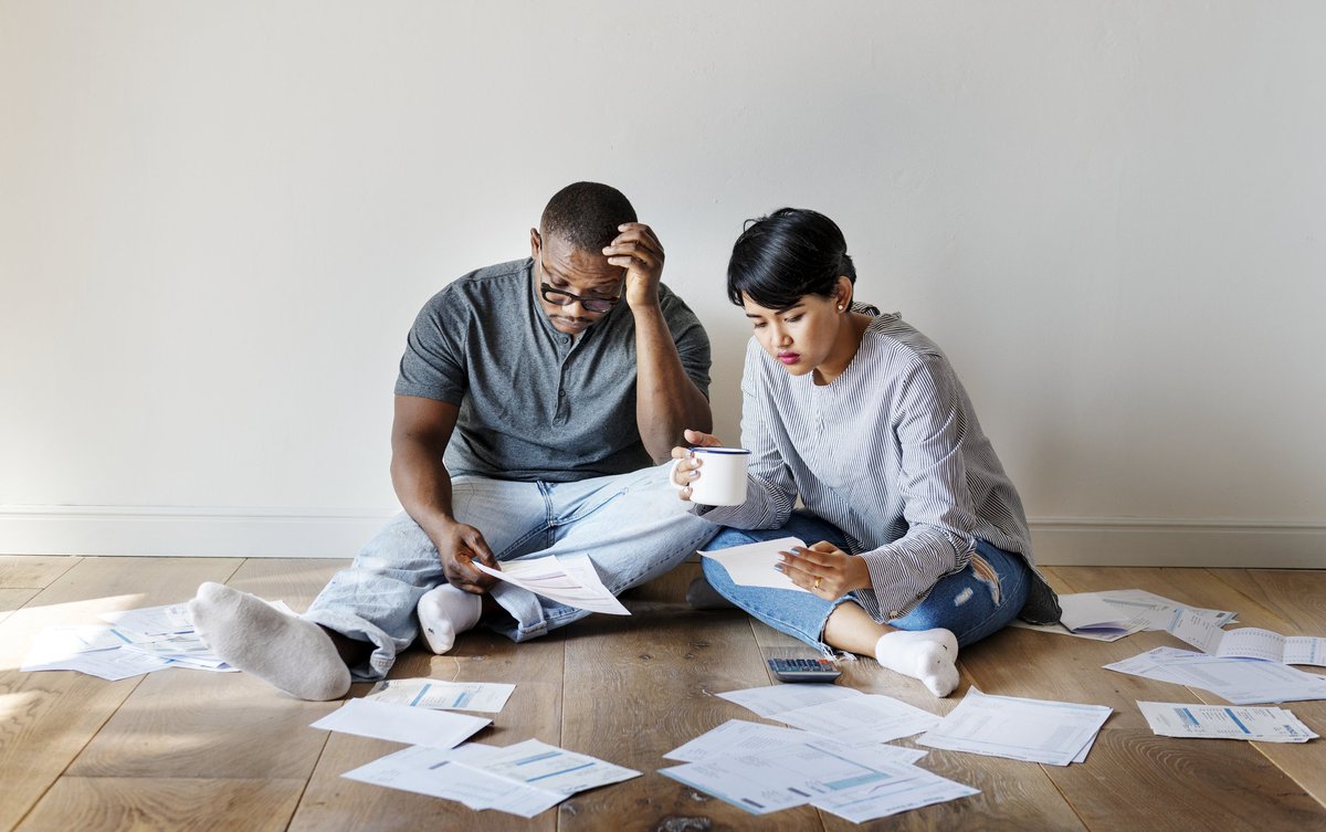 An upset young couple sitting on the floor looking through bills.