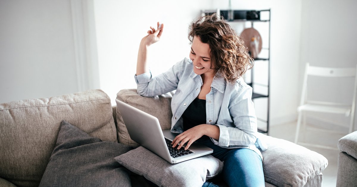 Woman on sofa sitting on laptop beaming in celebration.