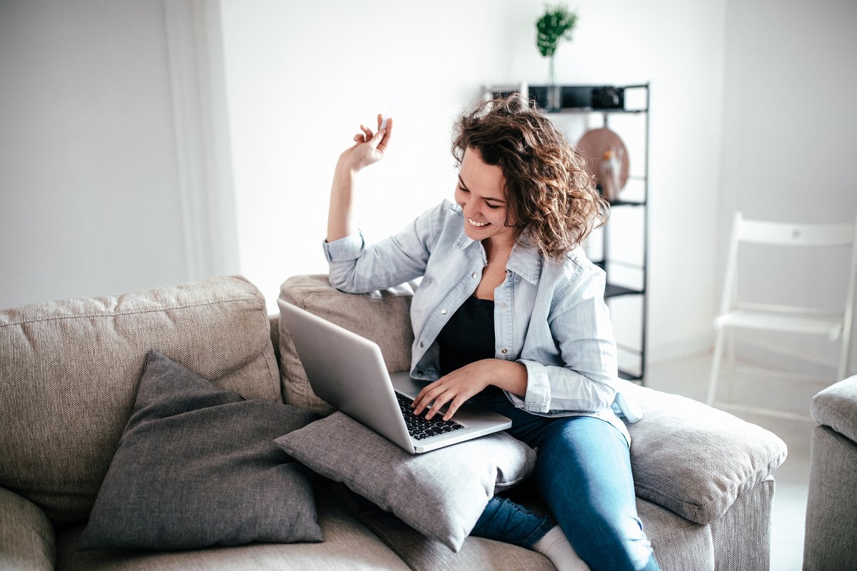 Woman on sofa sitting on laptop beaming in celebration.