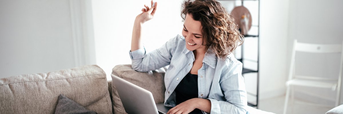 Woman on sofa sitting on laptop beaming in celebration.