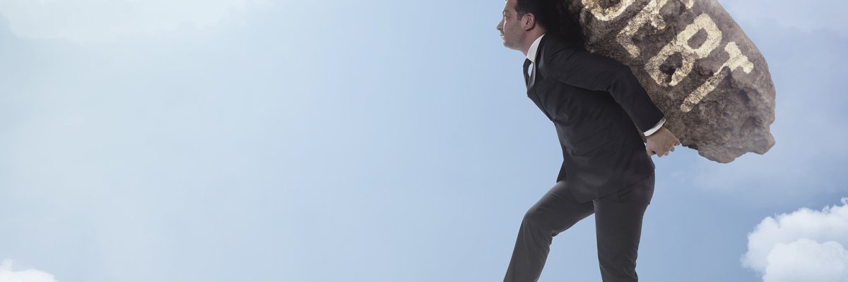 Man in suit carrying boulder labeled DEBT to edge of cloudy precipice.