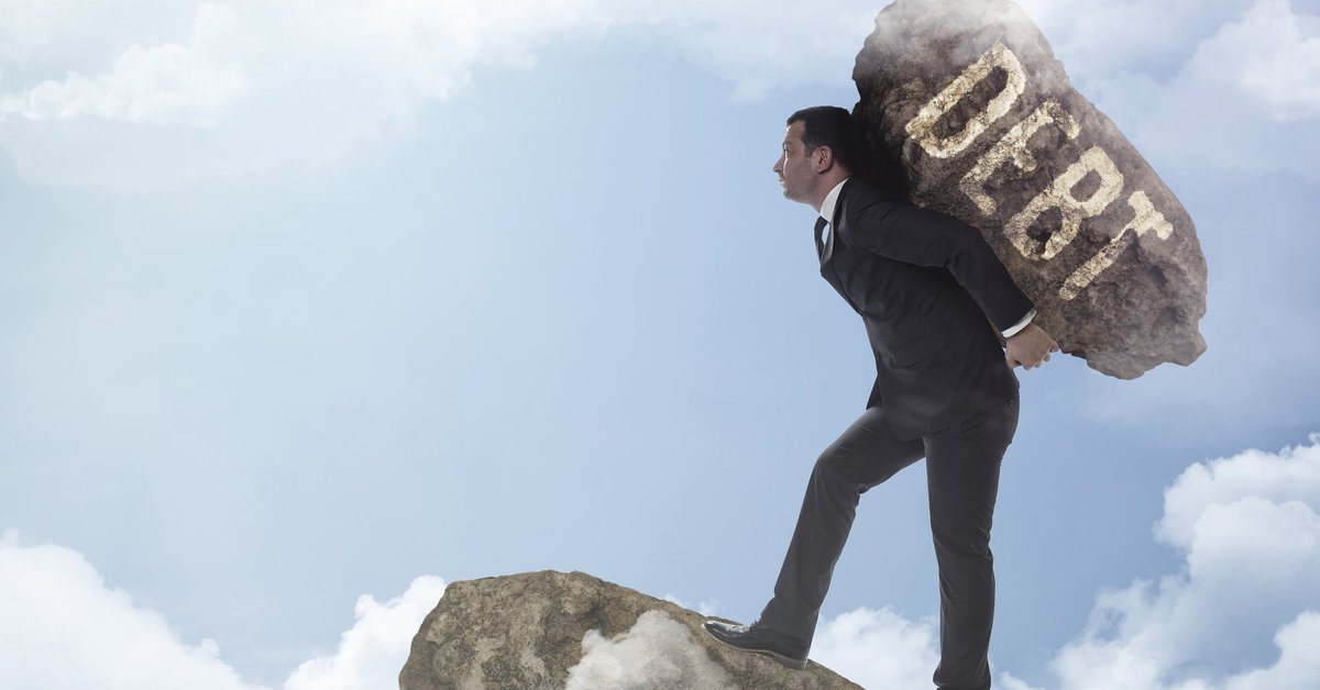 Man in suit carrying boulder labeled DEBT to edge of cloudy precipice.