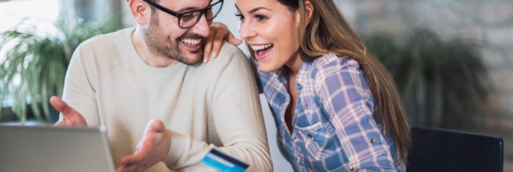 Happy couple with laptop holding a credit card and gesturing toward the screen.