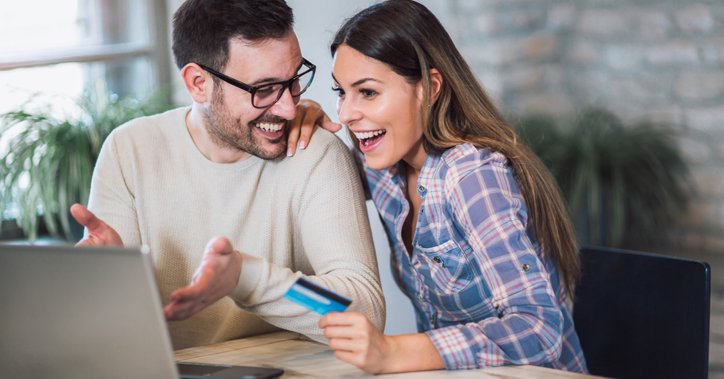Happy couple with laptop holding a credit card and gesturing toward the screen.