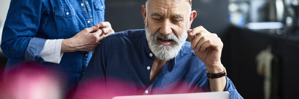 An older couple discusses something on a laptop screen.