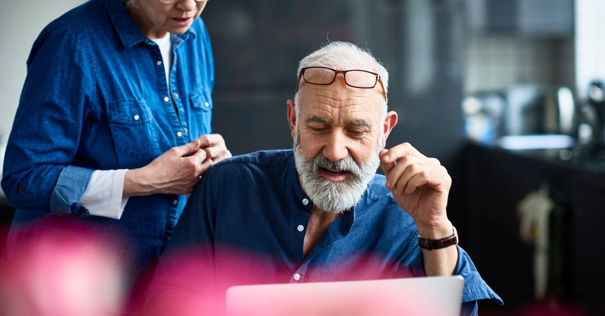 An older couple discusses something on a laptop screen.
