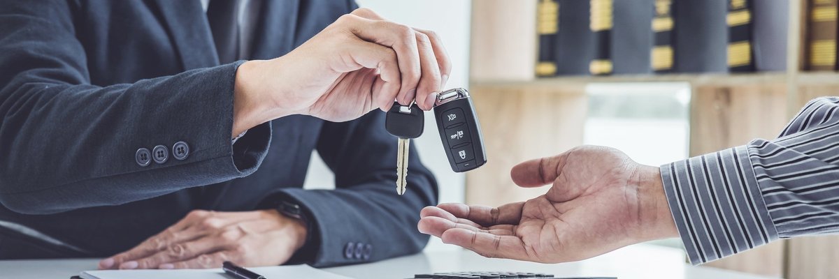 Man in suit reaching across desk to drop car keys into other person's hand.