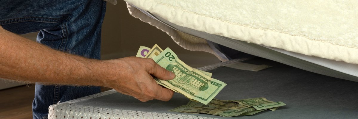 Man's arm hiding wad of cash under mattress.