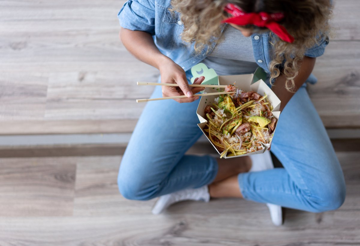 Crosslegged woman eats takeout with chopsticks.