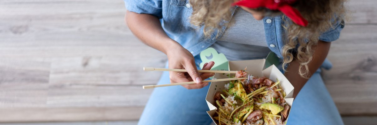 Crosslegged woman eats takeout with chopsticks.