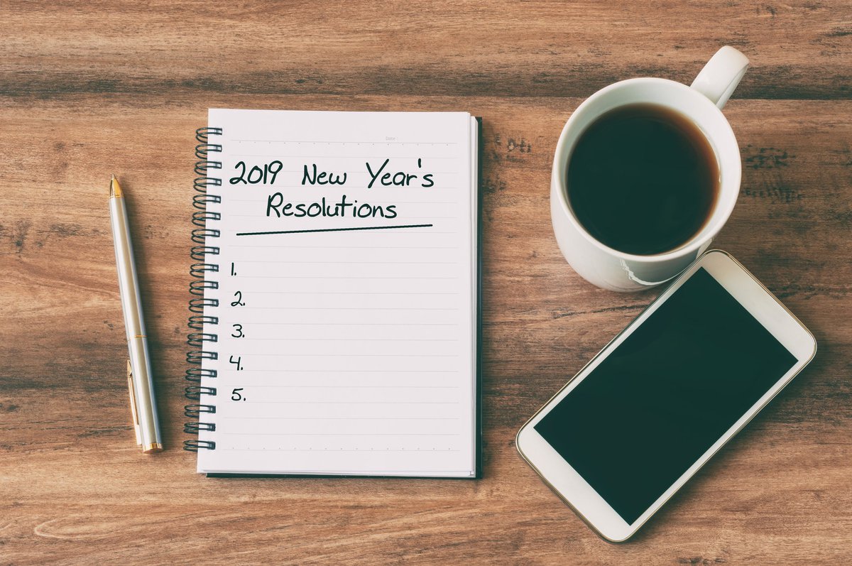 Cup of coffee, smartphone, pen, and notepad for 2019 New Year's Resolutions.