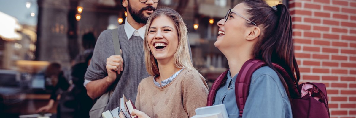 Three Students Walking Together Carrying Their Books And Laughing