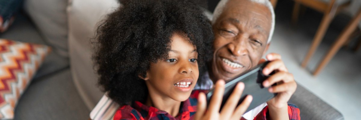 A grandparent watches as a grandchild plays a game on a phone.