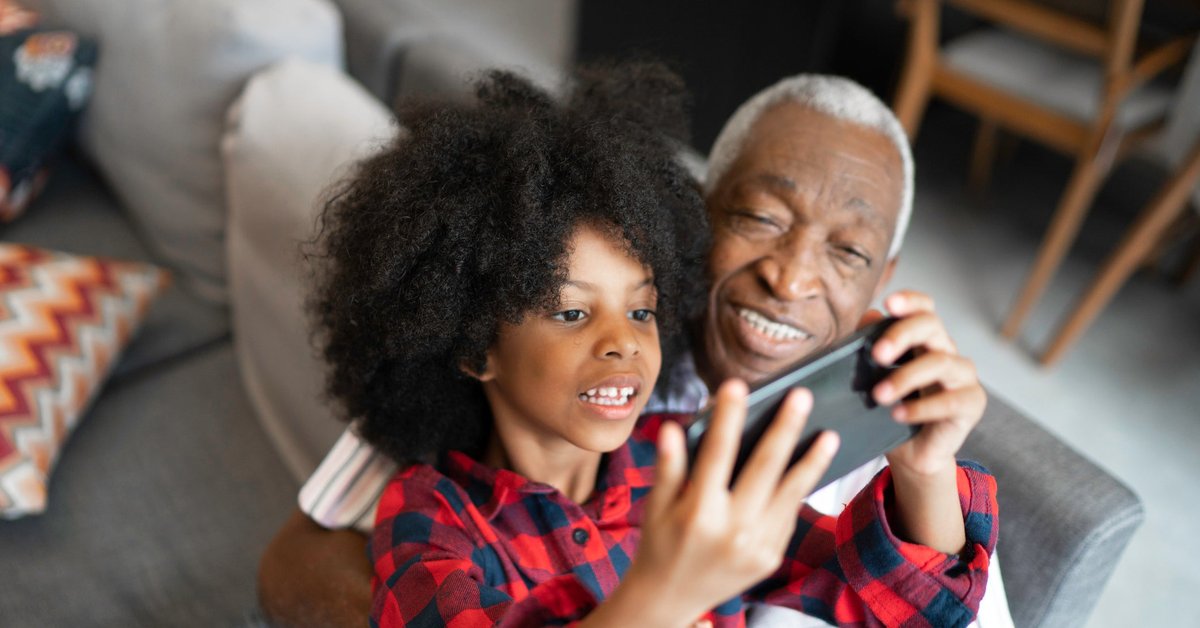 A grandparent watches as a grandchild plays a game on a phone.