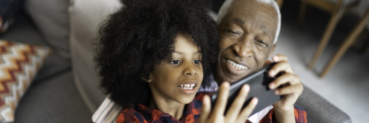 A grandparent watches as a grandchild plays a game on a phone.