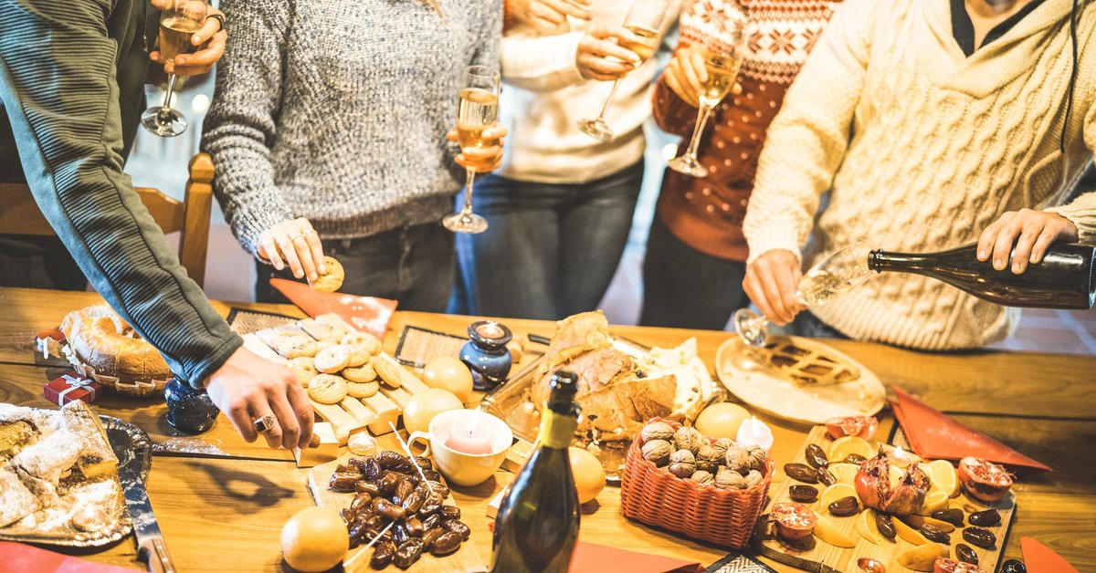 A group of friends in holiday sweaters gathered around platters of food and Champagne.