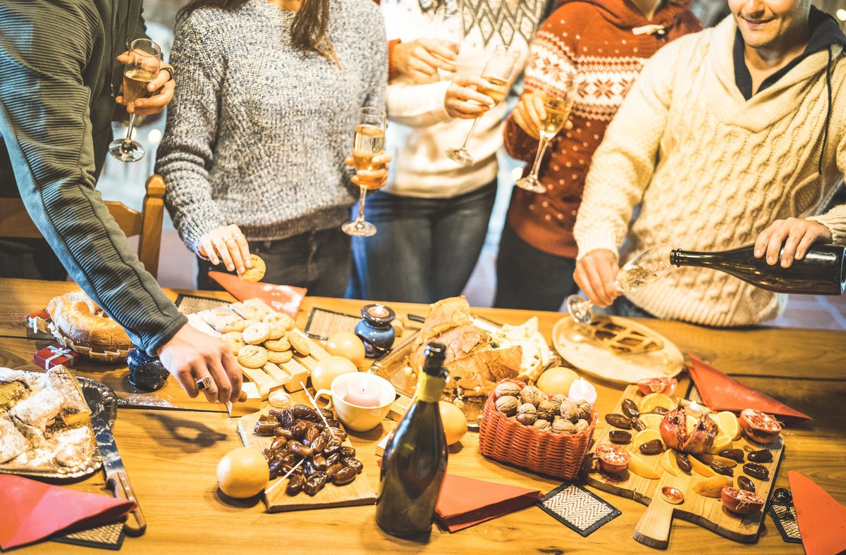 A group of friends in holiday sweaters gathered around platters of food and Champagne.