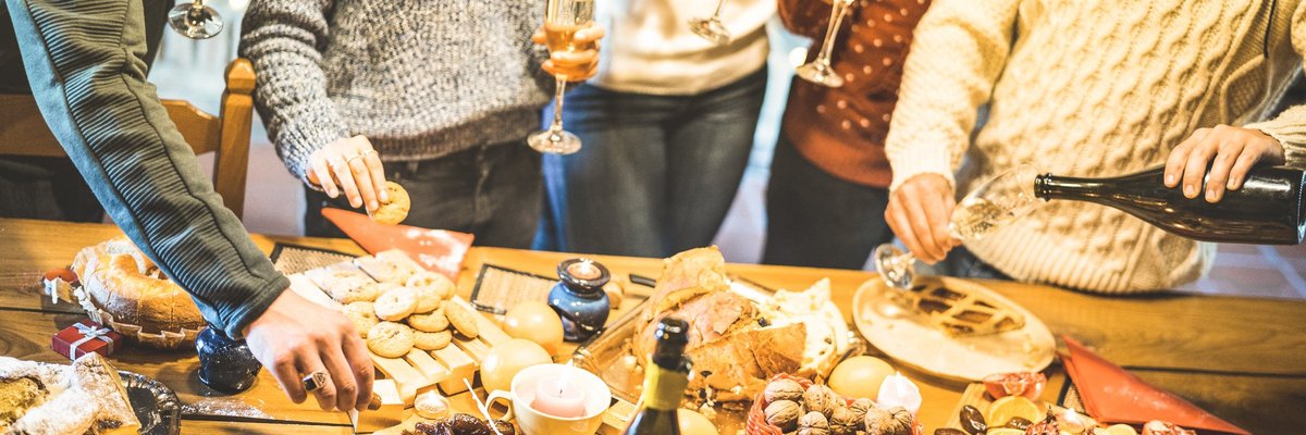 A group of friends in holiday sweaters gathered around platters of food and Champagne.