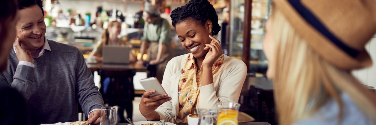 Group of friends enjoying food at a restaurant and using a mobile phone.