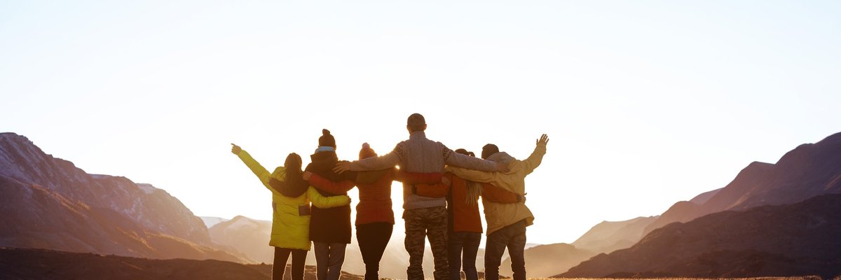 A group of friends looking at the sunset with their arms around each other.